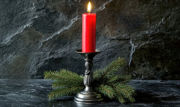 A candle is lit on a silver candle holder with a pine branch photo