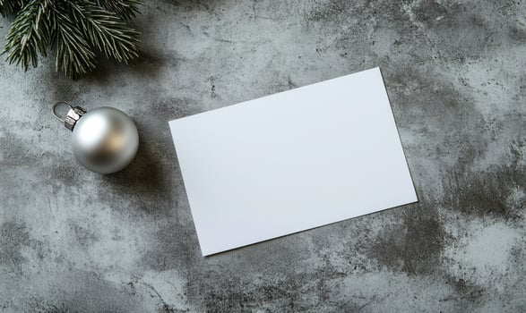 A white card sits on a grey surface with a silver ornament on top of it photo