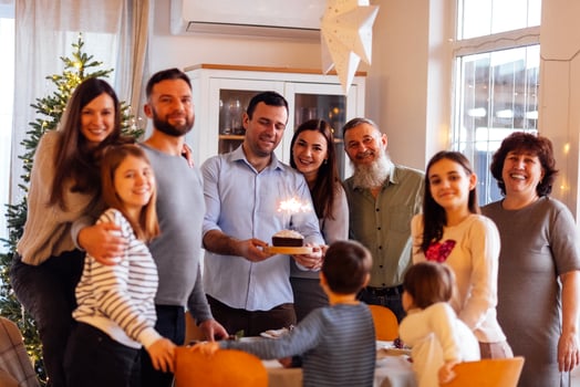 A big happy family at a festive table at home. An attractive young man with a cake with lighted sparklers and his smiling relatives in the living room. photo