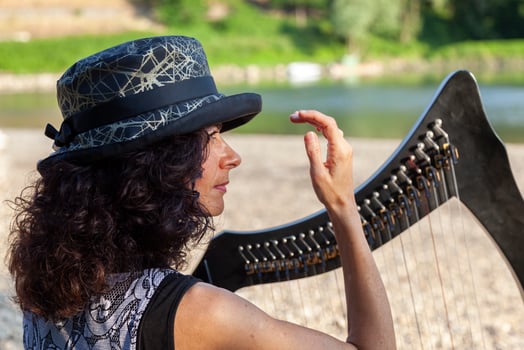 beautiful curly haired woman in fairytale clothes playing a small harp relaxing on a beach along the river at sunset photo