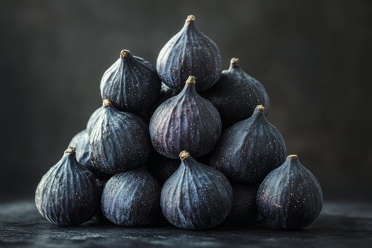 A pyramid of fresh dark figs arranged on a textured surface in a low light setting photo