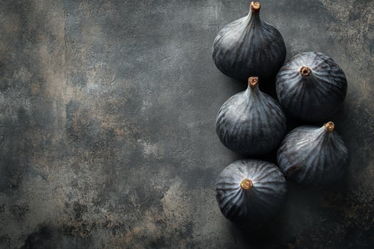 A pyramid of fresh dark figs arranged on a textured surface in a low light setting photo