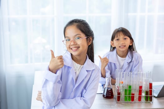 Two young asian students in scientific lab gown while studying science lesson in the classroom for education, literacy and tutoring concept with copy space photo