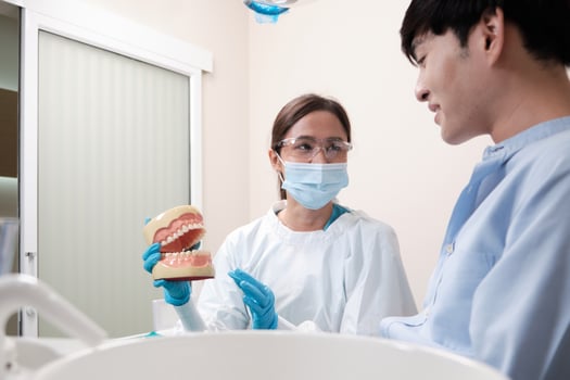 Asian female dentist explaining orthodontic care and whitening to young male patient with teeth model in dental clinic, well-being hygiene, and professional healthcare work in doctor office hospital. photo