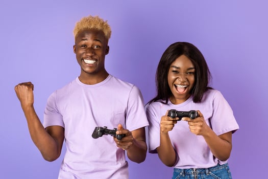 Fun hobbies concept. Cool black guy playing games with his girlfriend on lilac background. Panorama photo