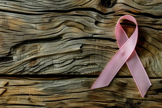 A pink ribbon rests on a weathered wooden table, representing awareness for breast cancer. This setting emphasizes hope and solidarity on a bright day photo
