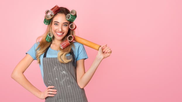 Housewife bakes concept. Happy girl with rolling pin on shoulder and apron smeared with flour photo