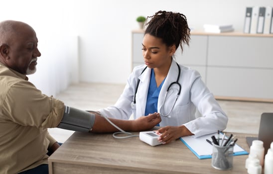 Hypertension In Older Age. Young Female Medical Worker Measuring Arterial Blood Pressure Of Senior Black Man Using Cuff, Patient Having Problems With Tension, Sitting At Table. Health Care Concept photo