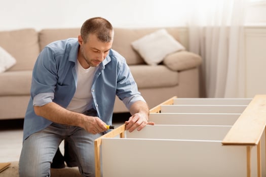 Middle-Aged Male Installing Wooden Cabinet Using Screwdriver At Home. Man Furnishing House Assembling Furniture Using Self-Assembling Shelf Kit. Furniture Assembly Concept photo
