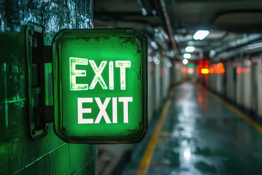 Illuminated red exit sign leading toward light in dark hallway photo