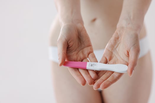 A woman shows a pregnancy test against her body in a bright bathroom photo