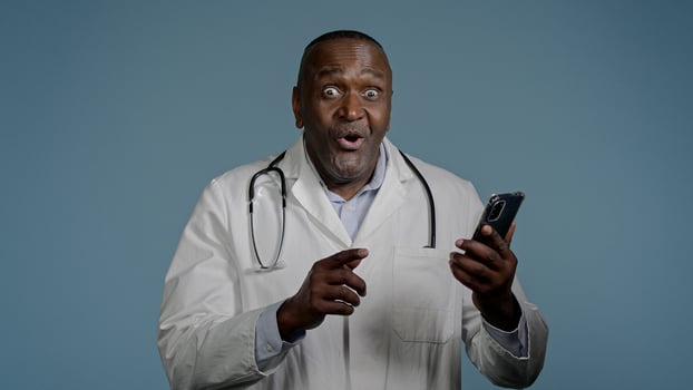 Happy African American man doctor male healthcare employee looking mobile phone screen receiving email reading good news excellent medical analysis result using smartphone in studio blue background photo