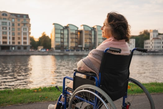 Sad senior woman sitting in wheelchair walking on road in city outdoor, back view. Old paralyzed lady in chair for people with disability feel depressed. Lonely elderly sick woman sits on wheelchair photo