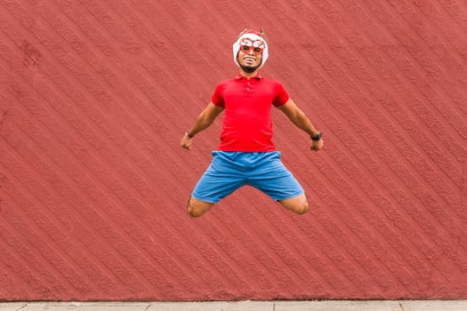 Hispanic man with christmas hat and glasses jumping on a street sidewalk, wall red, christmas concept. photo