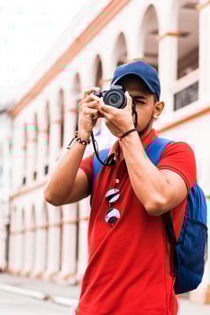 Young handsome beard man traveller in red shirt and backpack blue taking a photography outdoor on street. Traveller photographer concept. photo