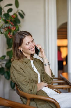 A cheerful woman talks on the phone in a cozy setting, surrounded by stylish decor and plants photo