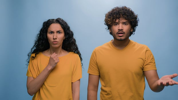 Multiracial shocked scared afraid couple amazed shocked Hispanic woman hiding behind Indian man astonishment wonder scare terrible horror ugly reaction blue studio background shock astonish fright photo