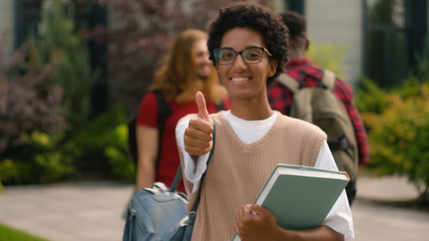 Students talking near university campus outdoors African American happy satisfied student girl woman showing thumb up like recommend gesture after class education with book good high school knowledge photo