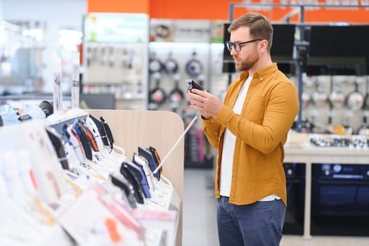 A bearded stylish man makes a choice while standing at a showcase with electronic trimmers and razors photo