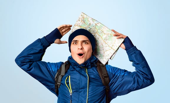 It's a miracle. Impressed young traveler with city map raising hands up over orange studio background photo