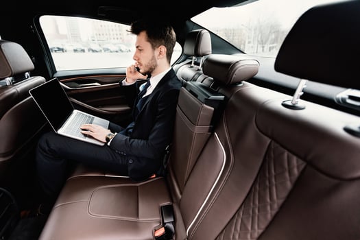 Business Travel. Busy chief executive in suit using laptop, making phone call in luxury car, side view photo