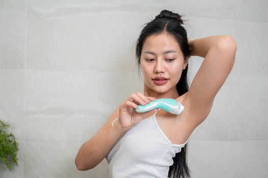 A beautiful Asian woman is shaving her armpit with a feminine razor in front of the mirror. photo