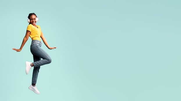 Joyful Black Woman In Headphones Jumping Smiling To Camera On Blue Studio Background. Copy Space photo