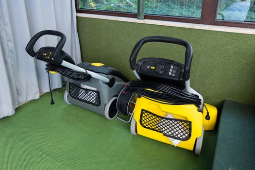 Two industrial vacuum cleaners sit on a green mat beside a window photo