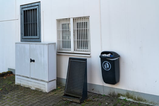 A gray utility storage unit stands beside a black waste bin attached photo