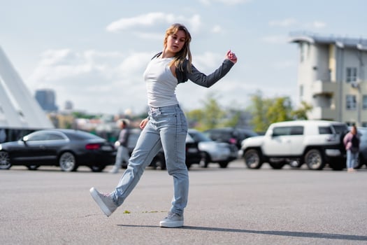 Young woman dancing in a parking lot on a sunny day with urban backdrop photo