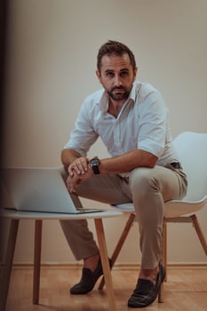 A confident businessman sitting and using laptop with a determined expression, while a beige background enhances the professional atmosphere, showcasing his productivity and expertise. photo