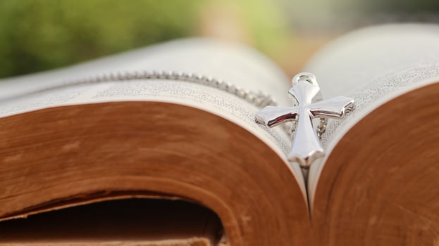 Shiny metal cross leaning against an old open book symbolizing the spread of Jesus Christs love among Christians reflecting faith devotion and the importance of Christian teachings. photo
