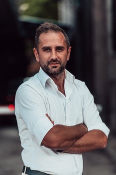 A successful businessman in a white shirt, with crossed arms, poses outdoors, confident expression on his face. photo