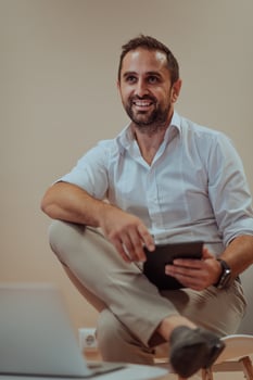 A confident businessman sitting and using tablet with a determined expression, while a beige background enhances the professional atmosphere, showcasing his productivity and expertise. photo