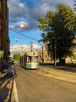 A vintage-inspired tram travels down a quiet street in Saint Petersburg, illuminated by the warm afternoon sunlight. The tram retro design harmonizes with the historic architecture of the city photo