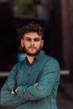 A successful young businessman in a shirt, with crossed arms, poses outdoors, confident expression on his face. photo