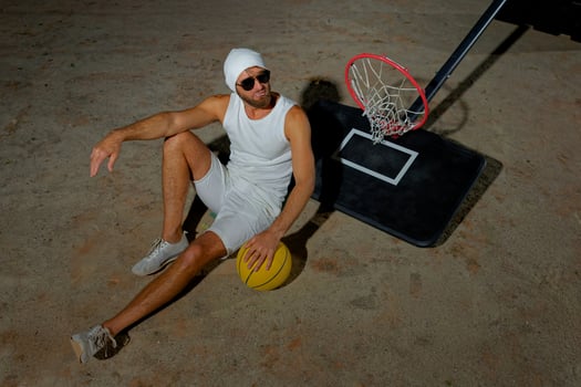 A basketball player sits on the court wearing sunglasses, relaxed after an intense practice session at dusk photo