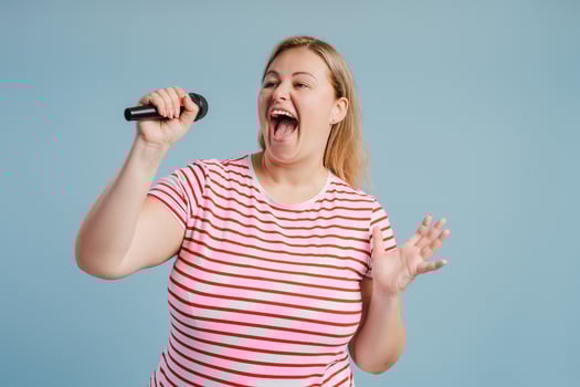 Young plus size Caucasian woman singing emotional with mic, isolated on blue photo
