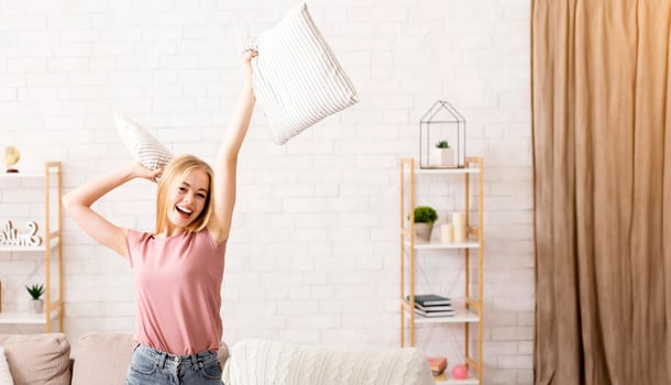 Happy young pretty woman having fun alone at home, dancing with pillows on couch, copy space photo