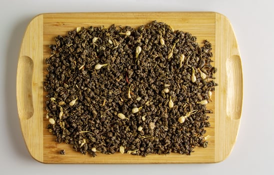 Green dry tea with jasmine flowers on a wooden board. Background and texture of dry tea. photo
