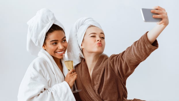 Multiethnic cheerful girlfriends taking selfie in bathrobes, having fun at home photo