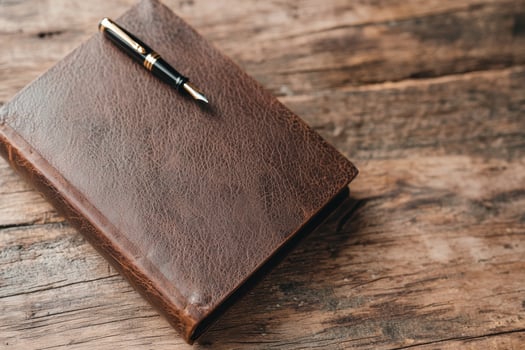 Leather bound journal and fountain pen on wooden table photo