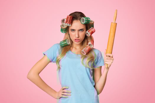 Strict housewife with curlers holds rolling pin, free space photo