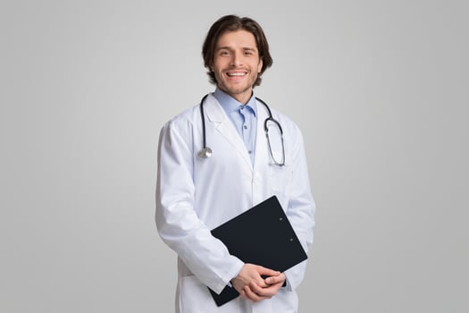 Medical Internship. Portrait Of Happy Male Doctor Student In Uniform Holding Clipboard In Hands And Posing Over Light Background, Panorama photo