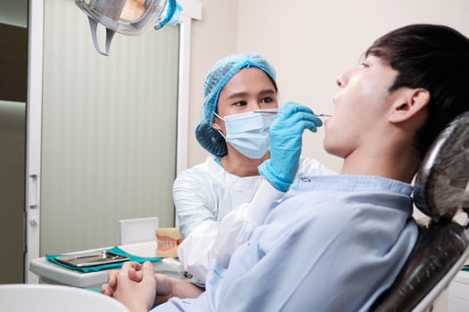 Asian female dentist examine young male patient teeth and toothache stomatology in dental clinic, well-being hygiene checks, and professional orthodontic healthcare work in doctor's office hospital. photo