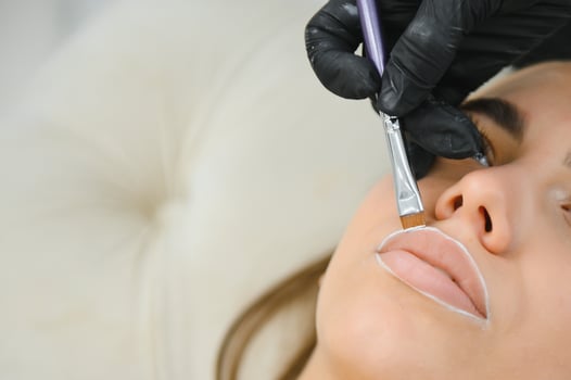 The permanent makeup artist draws a white outline on the lips before the procedure begins photo