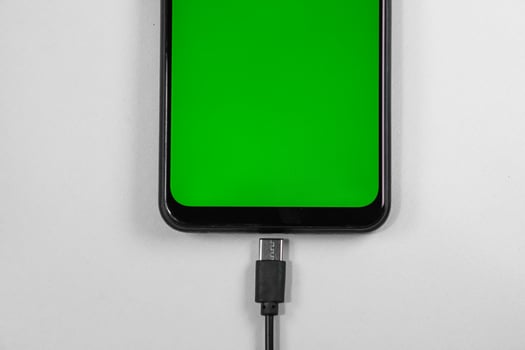 mobile phone with green screen connected to a charger on white background photo