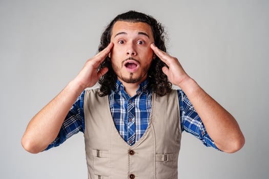 Young man with curly hair expresses surprise in a light-colored setting photo