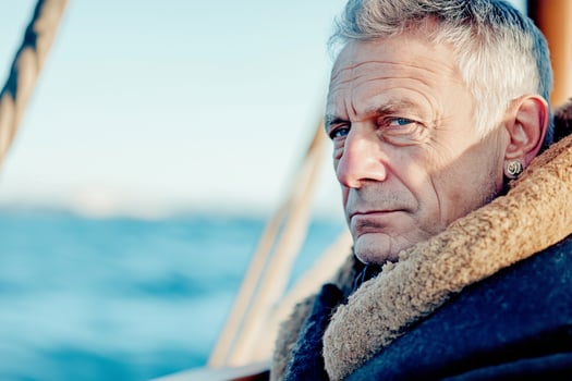 Old pirate with earring stands by ships helm at dawn overlooking the vast ocean horizon photo