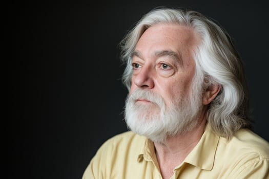 Elderly man with long white hair reflects thoughtfully against a dark architectural background photo